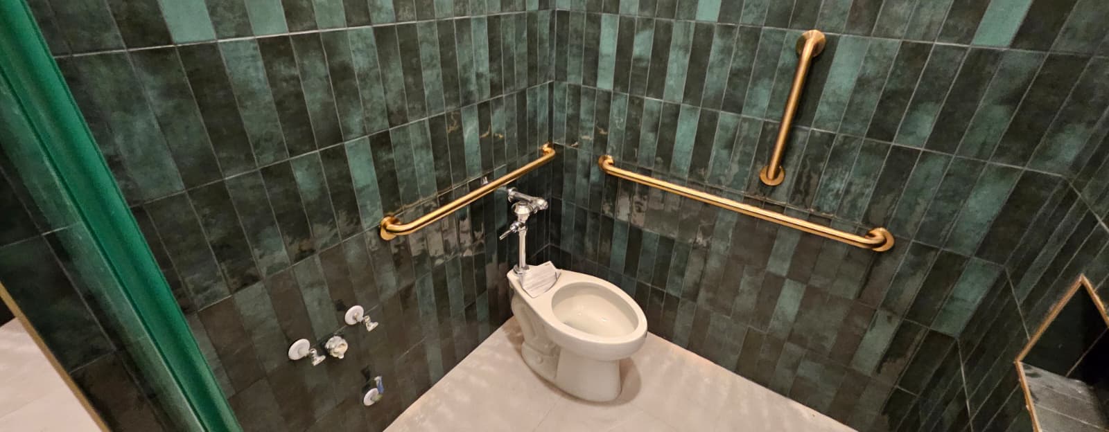 Solid-brass grab bars in a green tiled restroom at Casa Mezcal in Orlando, Florida